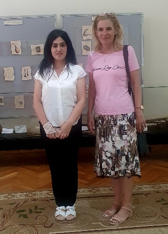 Local Azerbaijani artist standing beside her artwork displayed in a museum exhibition, showcasing traditional artistic techniques and cultural themes