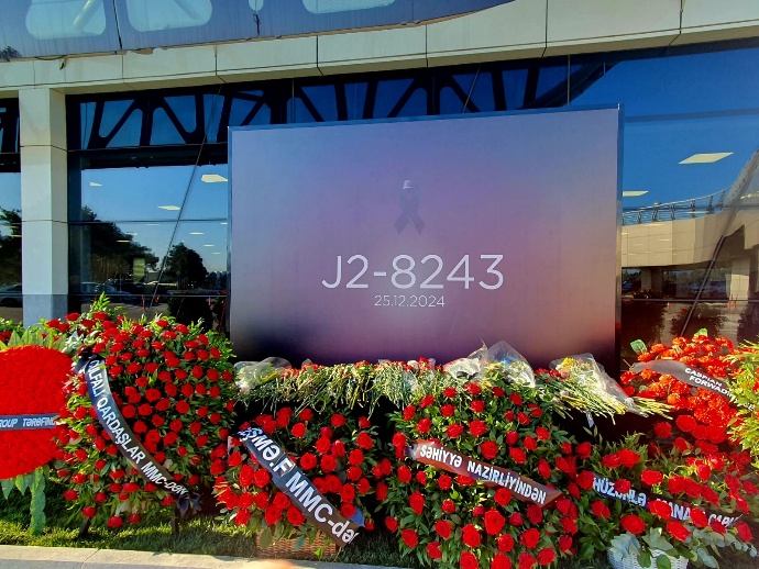 Memorial display honoring the victims of Azerbaijan Airlines Flight J2-8243, dated December 25, 2024, surrounded by red flower wreaths and tributes from various organizations at Heydar Aliyev International Airport in Baku, Azerbaijan.