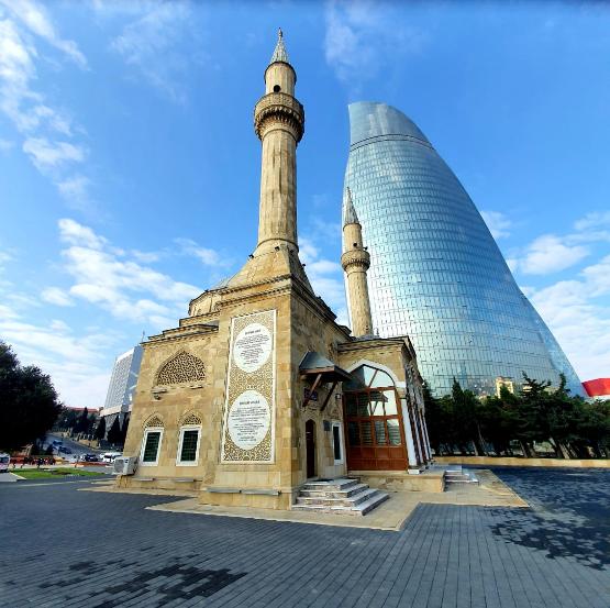 The Mosque of the Martyrs in Baku, with two tall minarets and ornate stone façades, viewed against the modern Flame Towers.