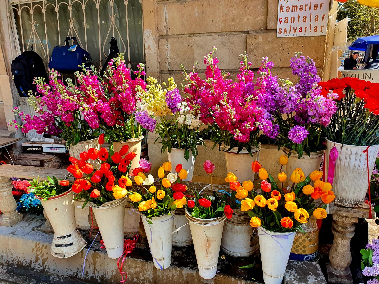 A vibrant street flower market in Icherisheher, Baku's Old City, displaying colorful bouquets of tulips and other flowers in white buckets