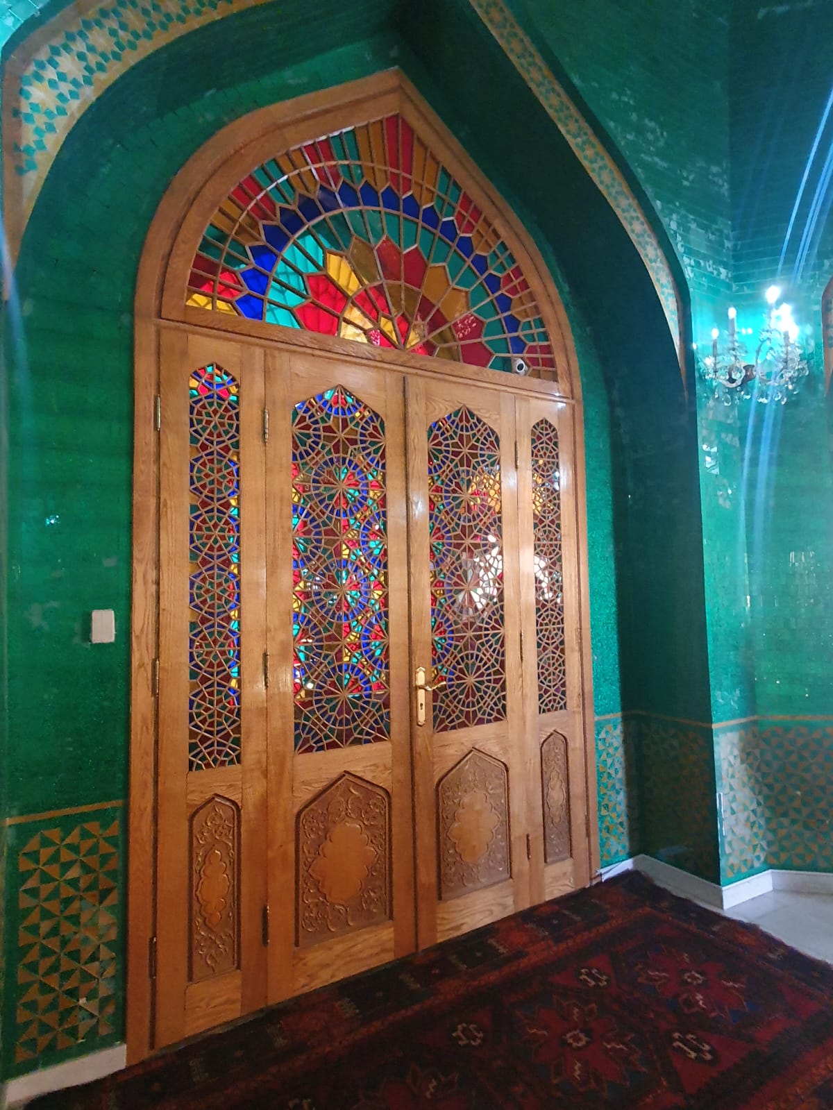 An ornately carved wooden door with colorful stained glass panels in arched frames at Bibi-Heybat Mosque in Baku, Azerbaijan
