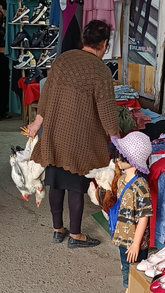 An elderly woman (grandmother) with her grandchild at a local Azerbaijani market, with live chickens visible in cages nearby