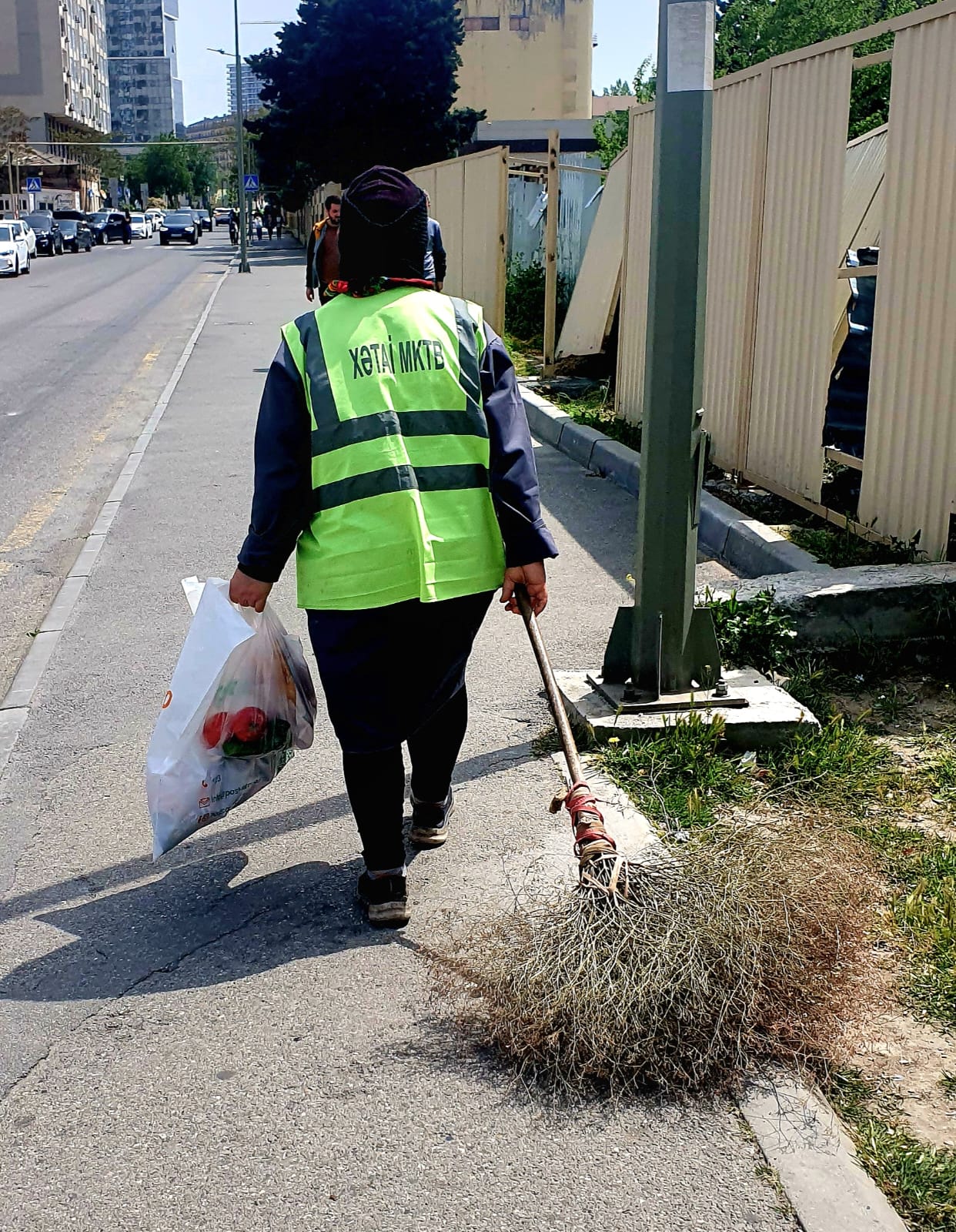 An elderly woman (babushka) working as a street cleaner in Azerbaijan, sweeping the pavement with a traditional broom
